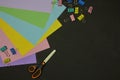 Top view of multicolor paper, paper clips and scissors on dark background with copy space. Back to school, education concept, Royalty Free Stock Photo