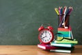 Back to school or education creative concept with red alarm clock, colorful notebooks and school supplies against blackboard Royalty Free Stock Photo