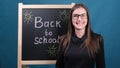 Back to school, a female teacher with glasses stands near the school blackboard and smiles