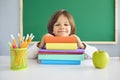 Back to school. Funny schoolboy looks at the camera while sitting at a table with books in a school classroom. Royalty Free Stock Photo