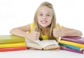 Back to school and happy time! Smiling schoolgirl sitting close to pile of books, showing Ok signs.