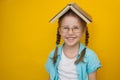 Back to school. Little beautiful girl in glasses with pigtails with an open book on her head smiles cute on a yellow background. Royalty Free Stock Photo