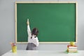 Back to school. Little schoolgirl writes on the school blackboard with chalk in the classroom.