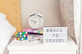 Back to school message with hashtag on lightened box with alarm clock, notebooks, rubik`s cube and stationery on the bedside tabl Royalty Free Stock Photo