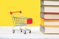 Back to school. A mini shopping cart and a stack of books with an open book at the top on a yellow background. Concept of Royalty Free Stock Photo