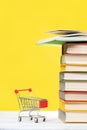 Back to school. A mini shopping cart and a stack of books with an open book at the top on a yellow background. Vertical. Concept Royalty Free Stock Photo