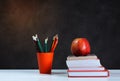 Back to school, orange pencil holder, stack of books on white table with red apple, empty black school board background, education Royalty Free Stock Photo