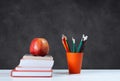 Back to school, orange pencil holder, stack of books on white table with red apple, empty black school board background, education Royalty Free Stock Photo