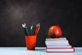 Back to school, orange pencil holder, stack of books on white table with red apple, empty black school board background, education Royalty Free Stock Photo