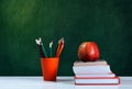 Back to school, orange pencil holder, stack of books on white table with red apple, empty green school board background, education Royalty Free Stock Photo