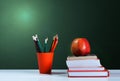Back to school, orange pencil holder, stack of books on white table with red apple, empty green school board background, education Royalty Free Stock Photo