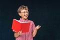 Funny smiling boy with glasses and book in his hand, posing on black background