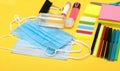 Back to school, school supplies with medical face mask and chat cardboard bubble on a yellow background. Protection of schoolchild