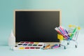 Back to school. School supplies in a grocery cart on a blue background near a black school board. Royalty Free Stock Photo