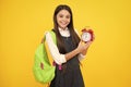 Back to school. Teenage school girl with backpack hold clock alarm, time to learn. Schoolgirl on isolated yellow Royalty Free Stock Photo