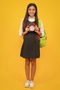 Back to school. Teenage school girl with bag hold clock alarm, time to learn. Schoolgirl on isolated yellow background Royalty Free Stock Photo