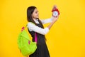 Back to school. Teenager schoolgirl with backpack hold clock alarm, time to learn. School children on isolated yellow