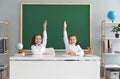 Back to school. Two adorable little girls sitting at desk and raising their hands, ready to answer lesson at classroom Royalty Free Stock Photo