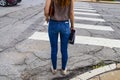 Back to school - Unidentifiable back of girl dressed in jeans with long red hair standing at crosswalk with notebooks and a leathe