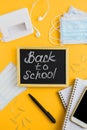 Chalk board, medical face masks, smartphone and school stationery on yellow background Royalty Free Stock Photo