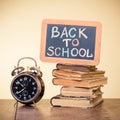 Back to School written on a blackboard, alarm clock, books on wooden table. Vintage style photo Royalty Free Stock Photo