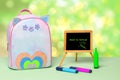 Back to school is written in green letters on a blackboard, colourful pencils and a colourful school backpack stand on a green Royalty Free Stock Photo