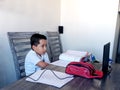 Back to school, 7 year old Latino boy in online home classes with laptop and school supplies Royalty Free Stock Photo
