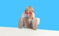 Back to shool banner. A little schoolboy with a dreamy expression is sitting at a white table on a blue fog. empty space