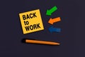 Back to work - concept of text on sticky note. Orange square sticky note, pen and colorful arrows on dark blue background, top