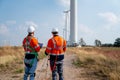 Back of two Caucasian engineers or technicians work in front of cluster of windmill or wind turbine for maintenance or manage