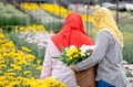The back of two Muslim worker girls are collecting the flowers in garden during day time with one girl wear red hijab and the Royalty Free Stock Photo