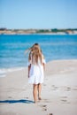 Back view of adorable little girl with long hair in white dress walking on tropical beach vacation Royalty Free Stock Photo