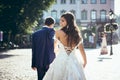 The back view of the adorable smiling brunette bride with bare back. The groom is leading her with the hand along the Royalty Free Stock Photo