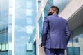 Back view of african american businessman walking along big office windows outdoors. Shot from back. Close up