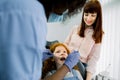 Back view of African female pediatric dental specialist making oral checkup of little curly red haired school girl Royalty Free Stock Photo