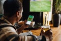 Back view of afro man watching football match and making bets at bookmaker\'s website while in front of TV screen Royalty Free Stock Photo