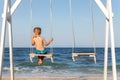 Back view of on alone cute little adorable small caucasian sad pensive kid boy swinging and playing at playground sea Royalty Free Stock Photo