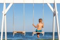 Back view of on alone cute little adorable small caucasian sad pensive kid boy swinging and playing at playground sea Royalty Free Stock Photo