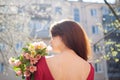 Back view of amazing and beautiful young woman holding a big bouquet of colorful flowers outdoors near the buildings on Royalty Free Stock Photo