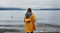 Back view of anonymous girl on raincoat standing on the sea shore. Generative AI