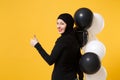 Back view Arabian muslim woman in hijab celebrating holding black white air balloons isolated on yellow background