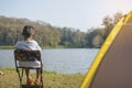 Back view of Asian child boy sitting on a chair for relaxing on camping in the tent with blur water resource and forest background