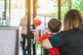 Back view of Asian little boy wear protective face mask in red shirt holding a toy with mother sit in waiting social distance