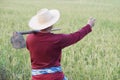 Back view of Asian man farmer wears hat, red shirt, carry a hoe on shoulder, point something at paddy field. Royalty Free Stock Photo