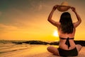 Back view of Asian plump woman wear bikini and hand holding straw hat sit on sand beach relax and enjoy holiday at tropical beach Royalty Free Stock Photo