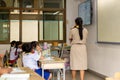 Back view of asian teacher stand in front of class and teaches students in school uniform.