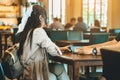 Back view of Asian woman with backpack holding wireless queue caller machine in hand to wait food in restaurant. Alarm signal