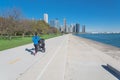 Back view of Asian woman running with stroller on lakefront road toward Chicago downtown