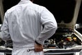 Back view of automotive mechanic in white uniform with wrench diagnosing engine under hood at the repair garage. Car insurance co Royalty Free Stock Photo