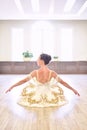 Back view of beautiful ballerina in cream dress sitting and warms up her hands on wooden floor in ballet studio Royalty Free Stock Photo